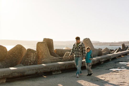 A young father with a small toddler son outdoors fishing by a sea