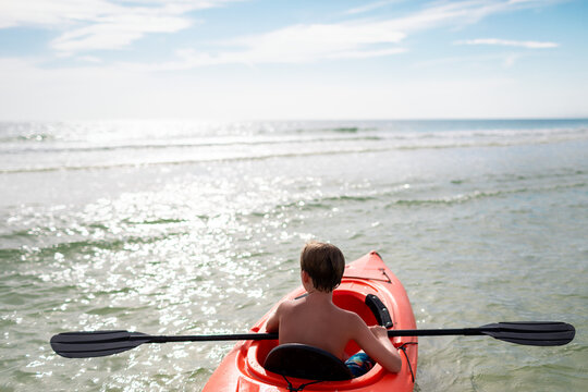 Child kayaking in calm ocean waters on sunny day
