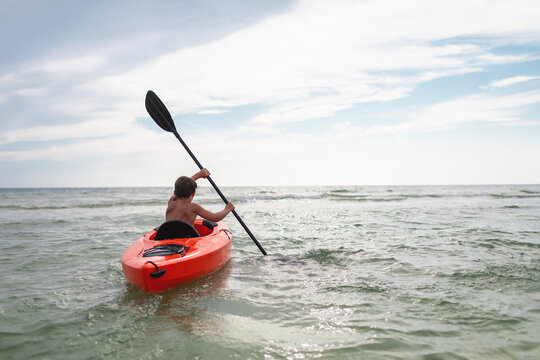 Boy paddling an ornage kayak in the vast blue ocean