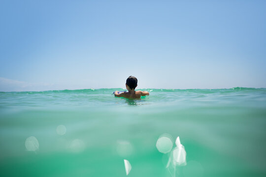 Young boy swimming in sun-drenched emerald ocean