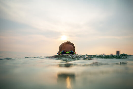 Child in goggles emerges from tranquil sunset waters
