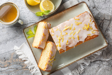 Glazed lemon pound cake loaf with lemon zest closeup on the plate on the table. Horizontal top view from above