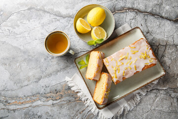 Lemon drizzle cake with lemon zest and icing is a classic British tea-time treat closeup on the plate on the table. Horizontal top view from above