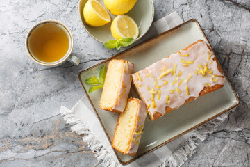 Homemade glazed lemon pound cake closeup on the plate served with tea on the table. Horizontal top view from above
