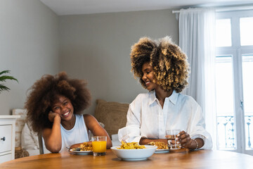 Image of cheerful family mother and little daughter smiling and eating together while having...