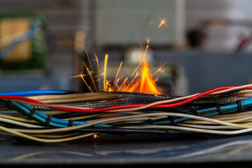 Flames, sparks, smoke between electrical cables, closeup. Short circuit in the twisted wires from the electrical devices, fire hazard concept - 793669215