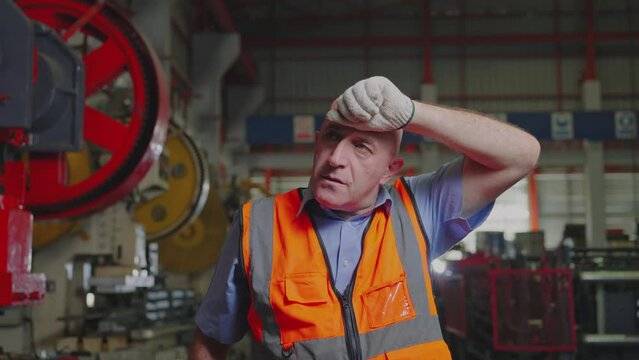 A hardworking industrial worker takes a brief pause to wipe sweat from his brow, reflecting the effort and dedication in a factory