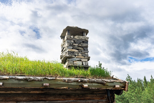 Scandinavian style roof with stone chimney decorated with plants. Оld traditional Norwegian wooden house roof covered with grass to insulate, sound insulation and protect from rain, snow and moisture.