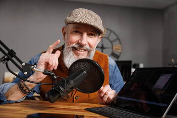 Studio podcast avec un micro et un ordinateur tablette et un homme souriant au look stylé et vintage avec une barbe hipster - 793675420
