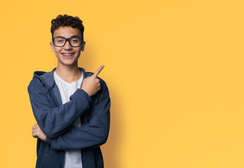 Excited happy black curly haired man in braces brackets, wear glasses, zipup hoodie jaket advertise show point sales slogan text area, isolate yellow background. Dental care, ophthalmology ad. - obrazy, fototapety, plakaty