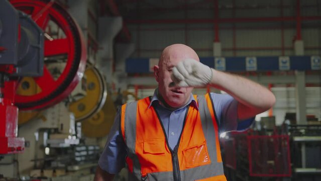 A hardworking industrial worker takes a brief pause to wipe sweat from his brow, reflecting the effort and dedication in a factory, Slow Motion