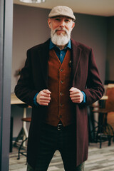Portrait d'un homme original gentleman quinquagénaire senior hispter élégant et stylé avec un manteau un béret et un gilet dans un atelier créatif - obrazy, fototapety, plakaty