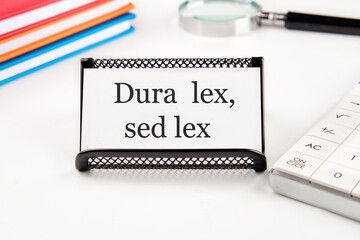Dura Lex Sed Lex. A Latin phrase meaning The law is harsh, but it is (still) the law. on a white business card on a table with office supplies - obrazy, fototapety, plakaty