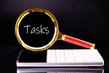 Business concept. TASKS - word through a magnifying glass on a black background in white font
