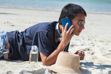 young man with headphones talking on the phone on the beach