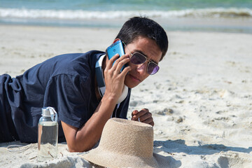young man with headphones talking on the phone on the beach