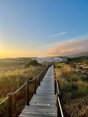 Explore the rustic charm of Portugal's coastline with a wooden bridge at sunset. Bask in the beauty of nature's hues blending seamlessly over sandy shores and tranquil waters