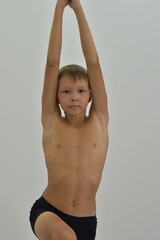 A fair-haired boy stands in a yoga pose with his arms raised. - obrazy, fototapety, plakaty