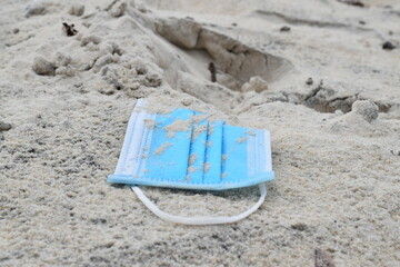 A blue medical mask against the virus is buried in white sand. - obrazy, fototapety, plakaty