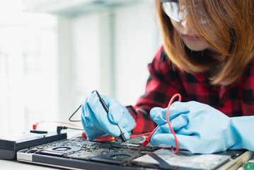 Focused technician with safety glasses repairing an electronic laptop motherboard in a laboratory setting.