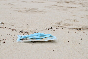 A dirty blue medical mask lies on the white sand. - obrazy, fototapety, plakaty