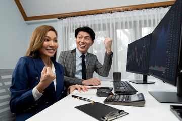 Successful smiling Asian business partners raising fist up together in profitable project job in...