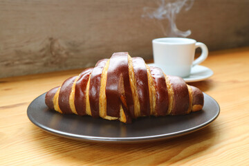 Delectable Chocolate Croissant with a Cup of Steaming Aromatic Coffee in the Backdrop