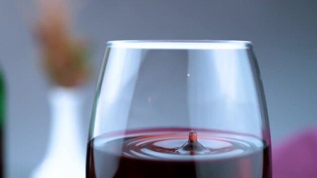 Captivating slow-motion shot showcases a single droplet of wine delicately descending into a partially filled glass, creating an elegant visual spectacle.