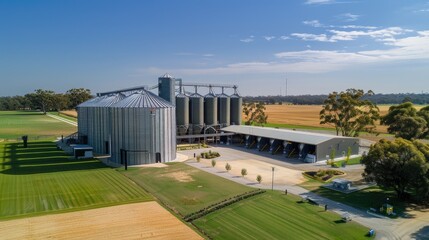 An overhead view of grain silos at an industrial farm, with blue sky and green fields in the background.