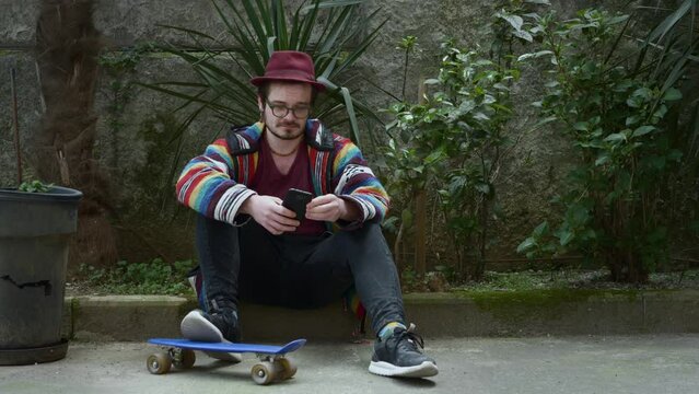 Stylish Man Sitting with Smartphone and Skateboard.