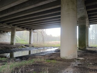 Concrete bridge and river. Concrete bridge. Small river floating under the bridge. Grass and trees around. Cloudy day. Countryside.