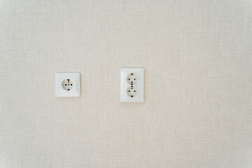 Two white electrical outlets are mounted on a beige wall