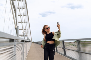 Urban woman takes a selfie while walking pedestrian bridge in city.