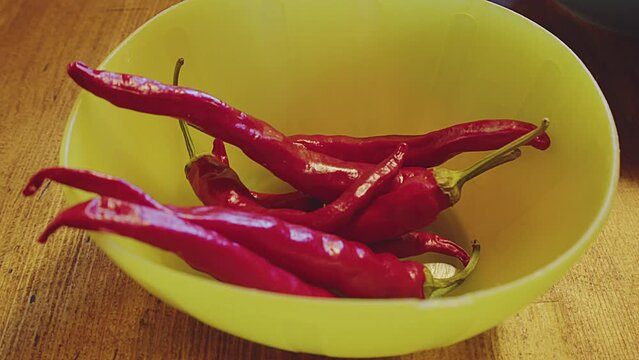 Close up of red chilli peppers in a blue plastic bowl on a wooden table. Kitchen interior. Studio shot. High quality 4k footage