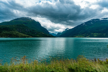 Mountain lake in Norway. Turquoise water of lake of glacial origin. Delightful amazing view of the landscape of Scandinavia northern Europe mountains. Beautiful glacier is visible in the distance.