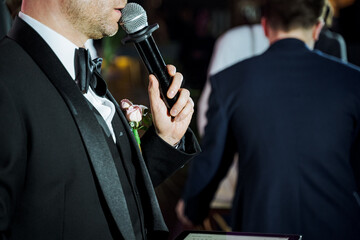 A man in formal wear with a tuxedo is holding a microphone