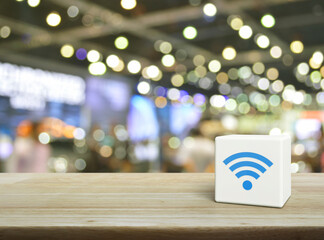 Wi-fi icon on white block cube on wooden table over blur light and shadow of shopping mall, Technology internet communication concept