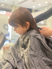  Side view of a young boy receiving a haircut from a stylist in a salon, covered with a cape.