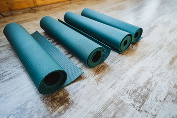 Three electric blue yoga mats neatly rolled on wooden floor
