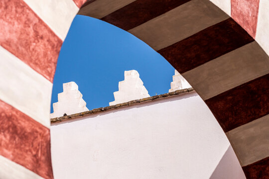 A close-up view of a structure in Cordoba, Andalusia, Spain captures the geometric shapes and contrasts between the red-striped arch and the sky, showcasing Europe's travel wonders