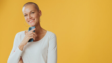 Smiling young hairless woman with mobile phone in her hands looking at camera, advertising space,...