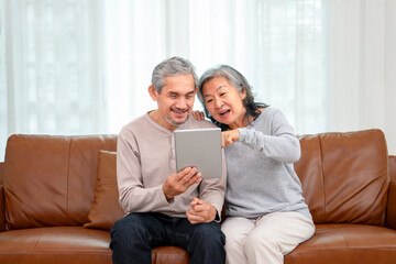 cheerful asian senior couple spend leisure time in living room together ,exciting while surfing online on their tablet computer,concept of elderly people modern lifestyle,internet,technology