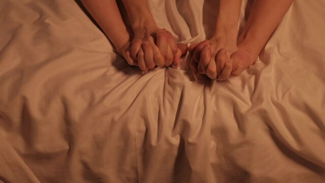 hands of woman and a man in sex on a white sheet on the bed in close-up. Couple having sex