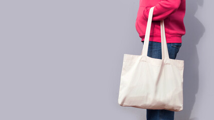 Woman in red hoodie holding tote canvas blank eco bag on street grey minimal wall background....