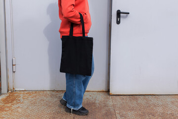 Woman in red hoodie holding tote canvas blank eco bag on street grey minimal wall background....