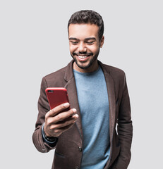 Portrait of handsome cheerful smiling young man using smartphone isolated on gray background. Laughing joyful men with mobile phone studio shot