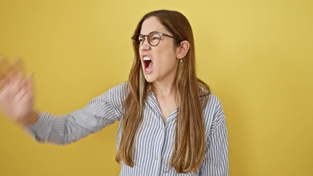 Furious young woman with blue eyes, screaming in aggression and frustration; enraged expression isolated in yellow background