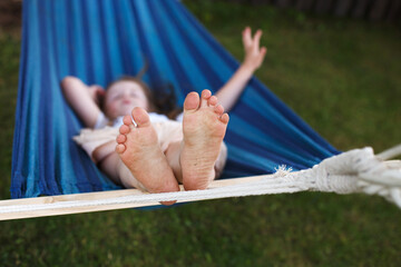 closeup of little girl's feet relaxing in the blue hammock during her summer vacation in back yard