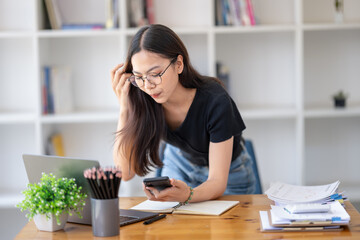 Cheerful young woman working on her laptop at a wooden table in a bright, plant-filled outdoor setting.