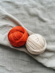 light orange and white colour two yarn ball and  background is a gray linen fabric.